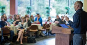 A person standing at a podium in front of a large room full of people.